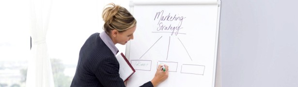 Businesswoman Writing on White Board and Businessman at Table --- Image by © Royalty-Free/Corbis